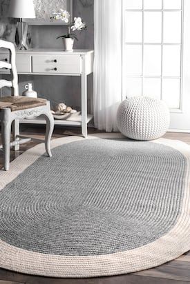 a living room with white furniture and gray rugs on the floor, along with an oval shaped area rug