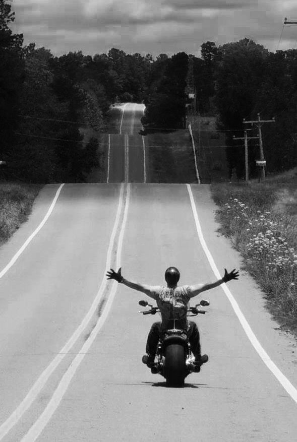 a man riding on the back of a motorcycle down a road with his arms outstretched