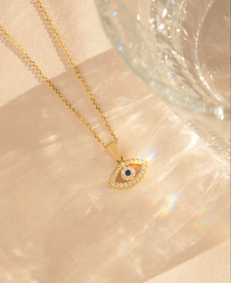 Evil eyes are an ancient symbol of protection. Know a Regina George in your life? Wear this daily to deflect the bad vibes. - 14k solid yellow gold - 16 inch chain length - Overlaid with cubic zirconia stones - Charm width: 13mm Spiritual Cubic Zirconia Necklaces With Diamond Accents, Gold Jewelry With Diamond Accents, Gold Cubic Zirconia Diamond Necklace, Gold Spiritual Necklace With Diamond Eyes, Gold Necklaces With Diamond Eyes In Round Pendant, Spiritual Yellow Gold Cubic Zirconia Jewelry, Gold Round Pendant Necklace With Diamond Eyes, Gold Plated Necklace With Diamond Eyes, Gold Spiritual Necklace With Diamond Accents