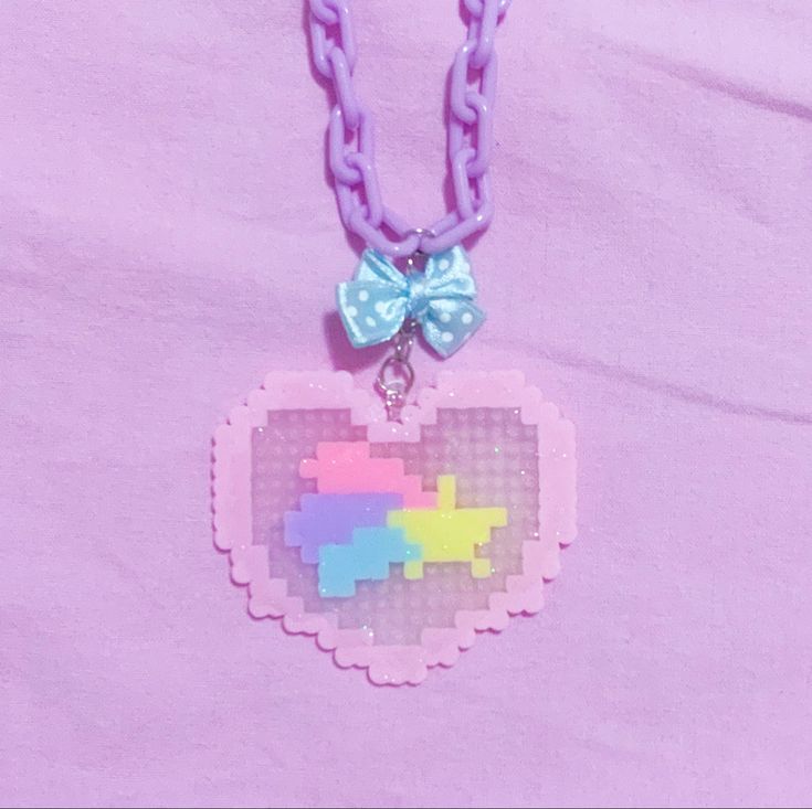 a necklace with a pixel heart on it and a bow hanging from the front, against a pink background