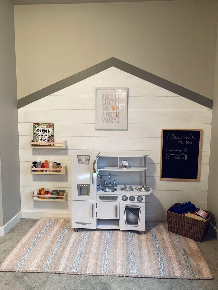 a toy kitchen set up in the corner of a playroom with shelves and toys