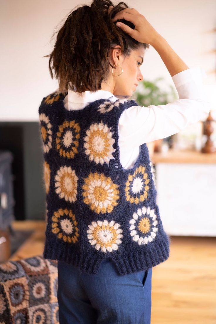 a woman standing in front of a fireplace wearing a blue sweater vest with flowers on it