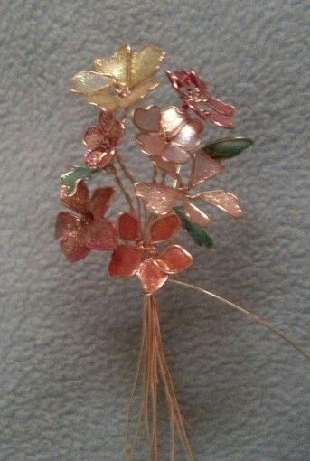 a close up of a flower brooch on a white surface with some green and red flowers