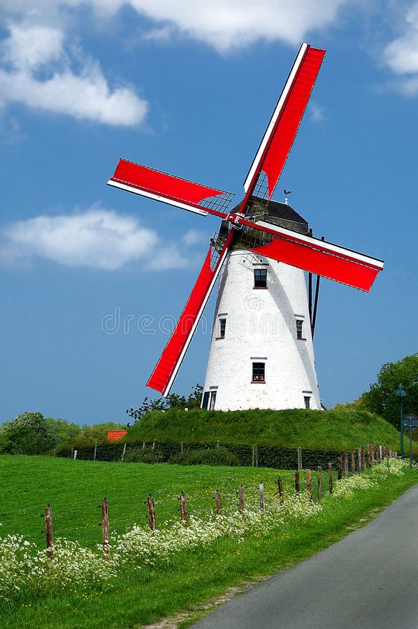 a large red and white windmill sitting on top of a lush green field next to a road