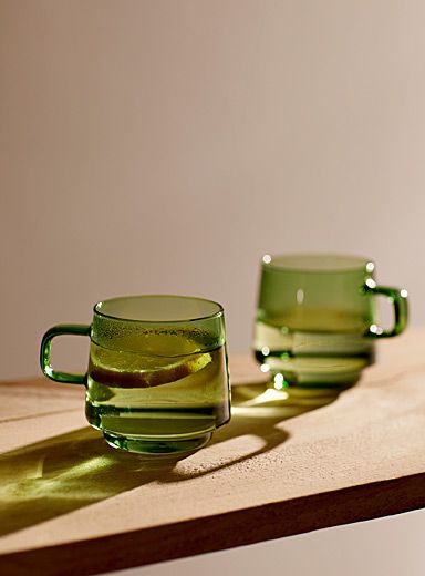 two green glass mugs sitting on top of a wooden table next to each other