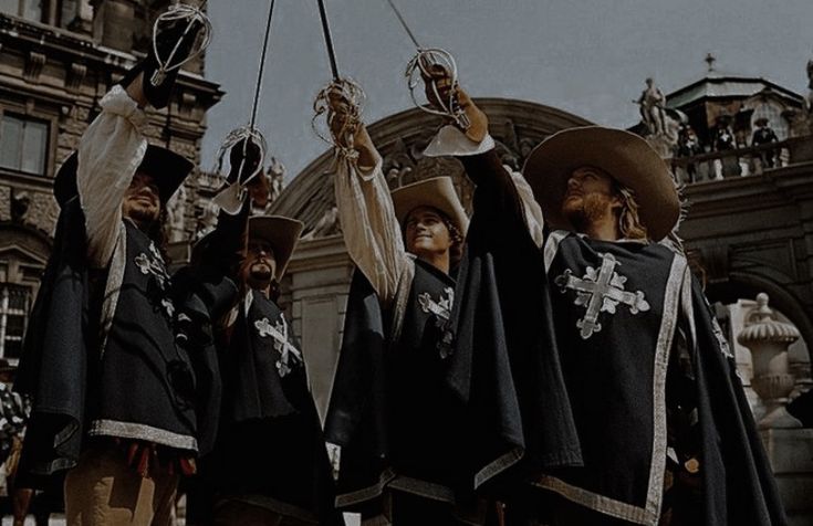 three men dressed in medieval clothing holding up their hands