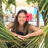 a woman is smiling while sitting in a palm tree with red flowers on her head