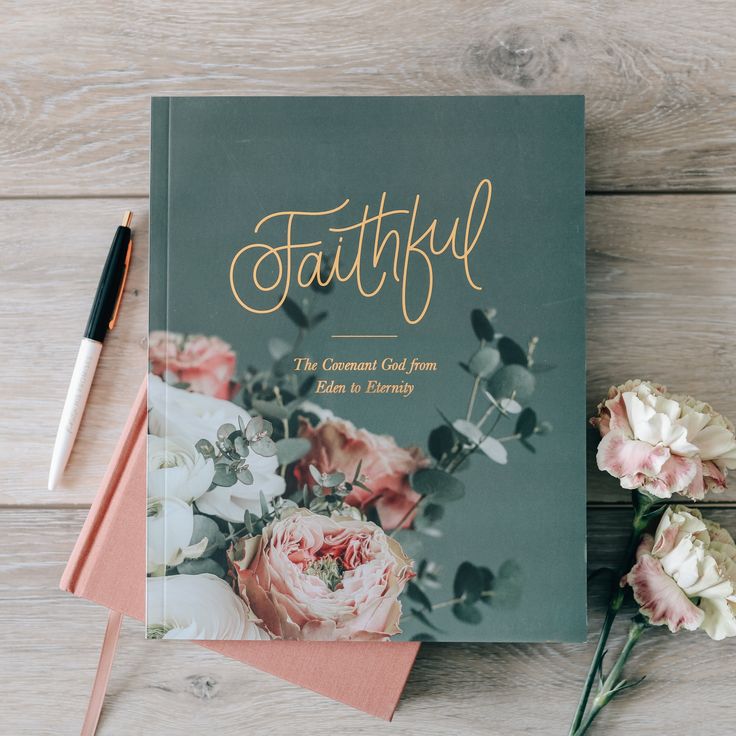 a book sitting on top of a wooden table next to some flowers and a pen