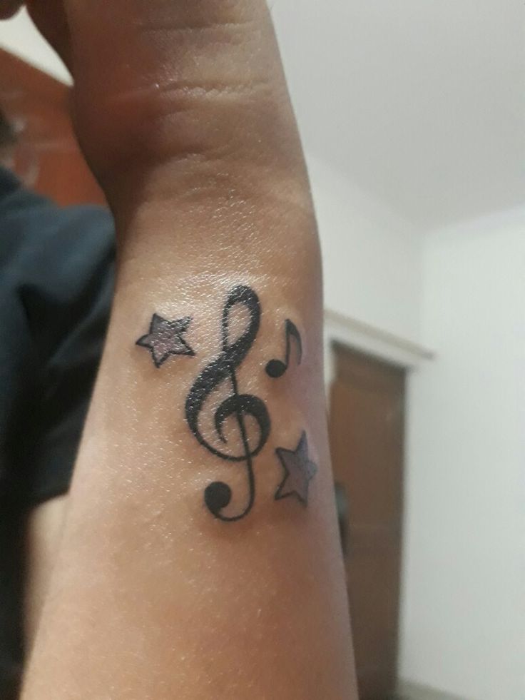 a person's wrist with a musical note and stars tattoo on the left arm