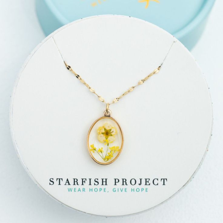 This necklace showcases the beauty of nature, in bloom. Dried yellow flowers are encased in clear resin within a 14K gold plated setting and an adjustable 14k plated gold chain, the In Bloom Necklace is perfect for everyday wear and layering alike. Shop the matching drop earrings Made in China Materials: 14k gold plated stainless steel chain with a yellow flower resin oval pendant necklace; Hypoallergenic; lead and cadmium free with nickel content less than 100 ppm Dimensions: chain is 16-18 inc Gold 14k Gold-filled Birth Flower Jewelry, 14k Gold Filled Birth Flower Jewelry, 14k Gold-filled Birth Flower Jewelry, Gold Jewelry With Birth Flower In 14k Gold Filled, Gold Flower Jewelry With Pressed Flowers, Gold Oval Jewelry With Flower Charm, Dainty Gold Jewelry With Pressed Flowers, Yellow Gold Flower Jewelry With Pressed Flowers, Yellow Gold Flower-shaped Jewelry With Pressed Flowers