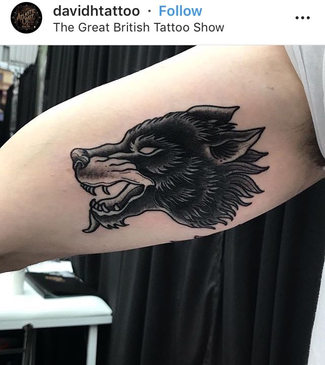 a black and grey wolf tattoo on the right arm with an arrow in it's mouth