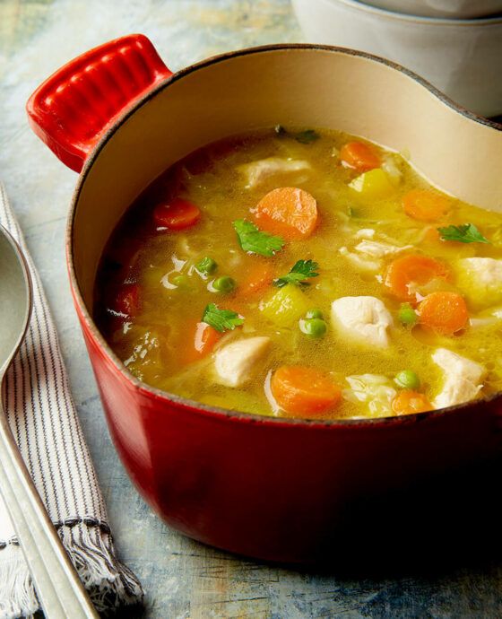 a red pot filled with chicken and carrots on top of a table next to a spoon