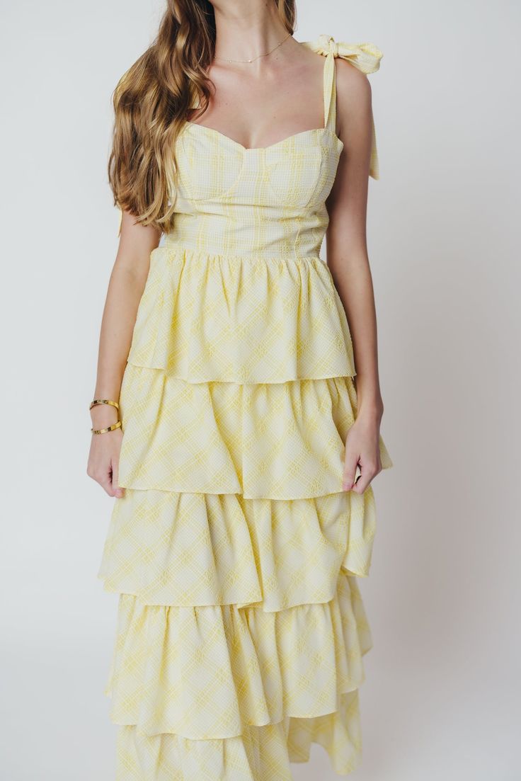 A stunning silhouette paired with summer-ready seersucker - the Jacquelyn Midi Dress has it all! This lovely gown is constructed from a textured, lightweight seersucker fabric in a playful plaid print, and features a sweetheart neckline, bustier bodice, and multi-tiered ruffle skirt. Pair with dainty heels for your next special event! FIT: Runs true to size. Bustier bodice is fitted, with a defined bust. MATERIAL: Hand wash cold, do not bleach. Line dry, do not tumble dry. Iron low if needed. GARMENT DETAILS: Plaid seersucker midi dress, with sweetheart neckline and bow-tie shoulder straps. Features a structured bustier-style bodice with defined bra, and a full skirt with multiple flounced tiers. SIZE GUIDE: S (2-4) / M (6-8) / L (10-12) MODEL DETAILS: Mackenzie - Size S Heather - Size S M Spring Gingham Sundress With Ruffles, Tiered Ruffle Hem Dress For Picnic, Gingham Plaid Dress With Ruffles For Daywear, Picnic Gingham Sundress With Ruffles, Plaid Daywear Dresses For Summer, Plaid Ruffled Dress For Picnic, Picnic Gingham Dress With Ruffles, Gingham Dresses With Ruffles For Picnic, Gingham Ruffled Dress For Daywear