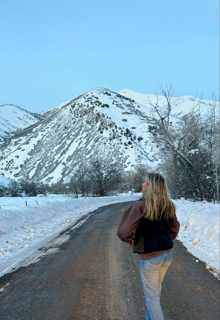 a woman is walking down the road in the snow with her back to the camera