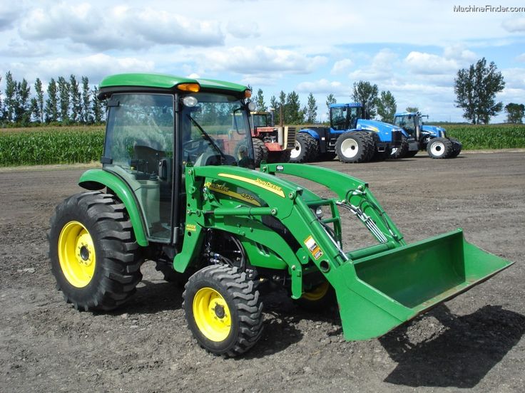 a green tractor parked on top of a dirt field next to two blue and yellow tractors