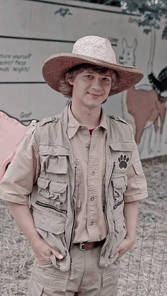 a man in a hat standing next to a wall