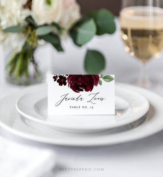 a place card is placed on a plate with wine glasses and flowers in the background