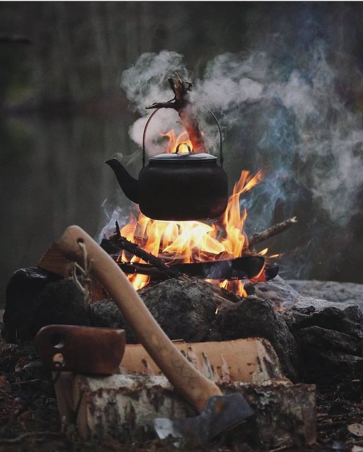 a tea kettle is on fire in the middle of some wood and logs with an ax sticking out of it