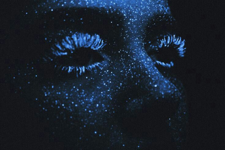 a woman's face is covered in blue glitter and her eyes are glowing bright