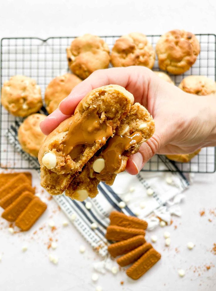 a person holding up a cookie with peanut butter on it and other cookies in the background