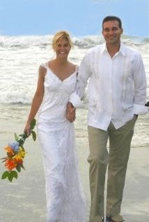 a man and woman are walking on the beach holding hands with each other while wearing white dresses