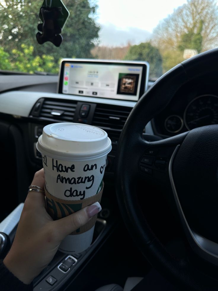 a person holding a cup of coffee in their hand while sitting in the driver's seat of a car