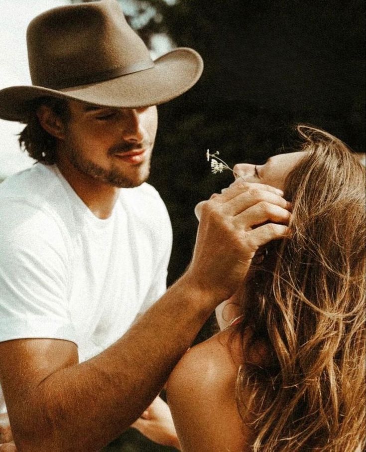 a man is fixing the hair of a woman with a cowboy hat on her head