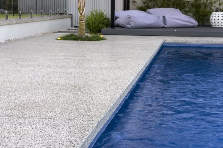 an empty swimming pool in front of a house with pillows on the floor and bedding