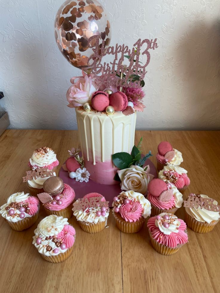 a table topped with lots of cupcakes next to a birthday cake and balloon