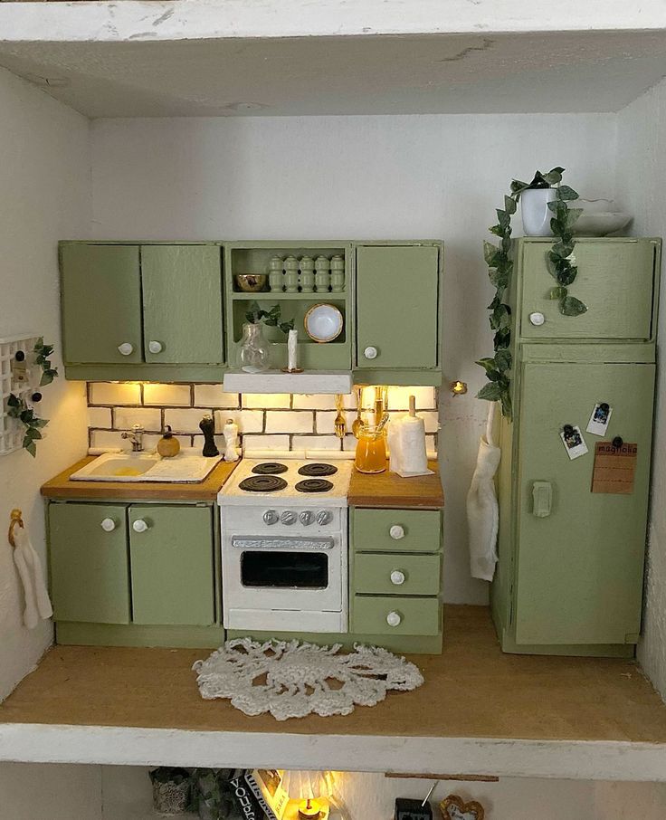 a dollhouse kitchen with green cabinets and white stove top oven, sink and refrigerator