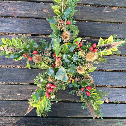 a cross made out of leaves and berries on top of a wooden bench with red berries