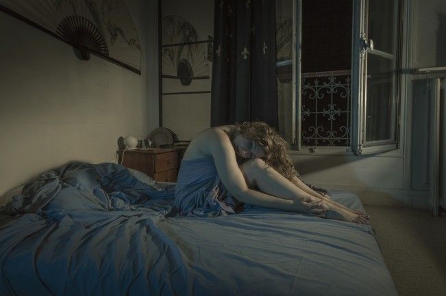 a woman laying on top of a bed covered in blue sheets next to a window