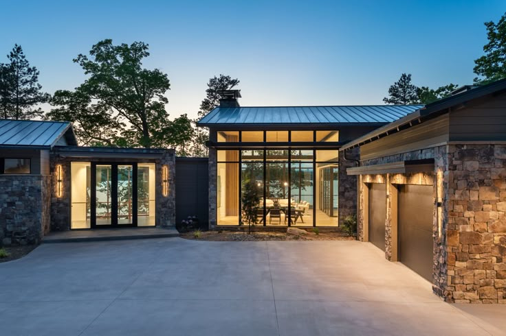 a modern house with stone and glass walls at dusk, lit up by lights on the windows