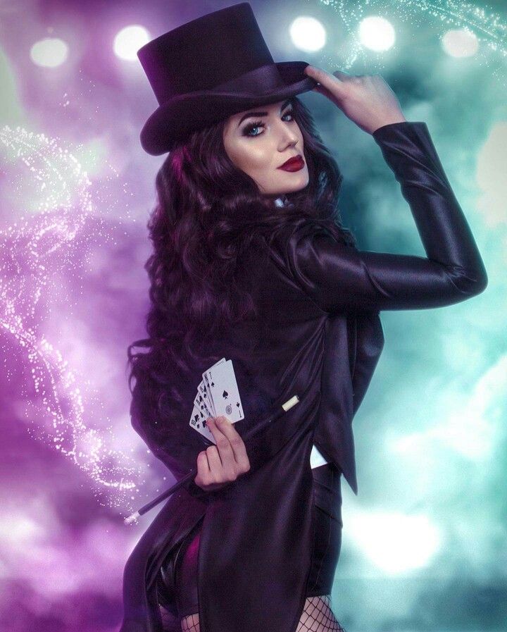 a woman in a black dress and top hat with cards on her lap, posing for the camera