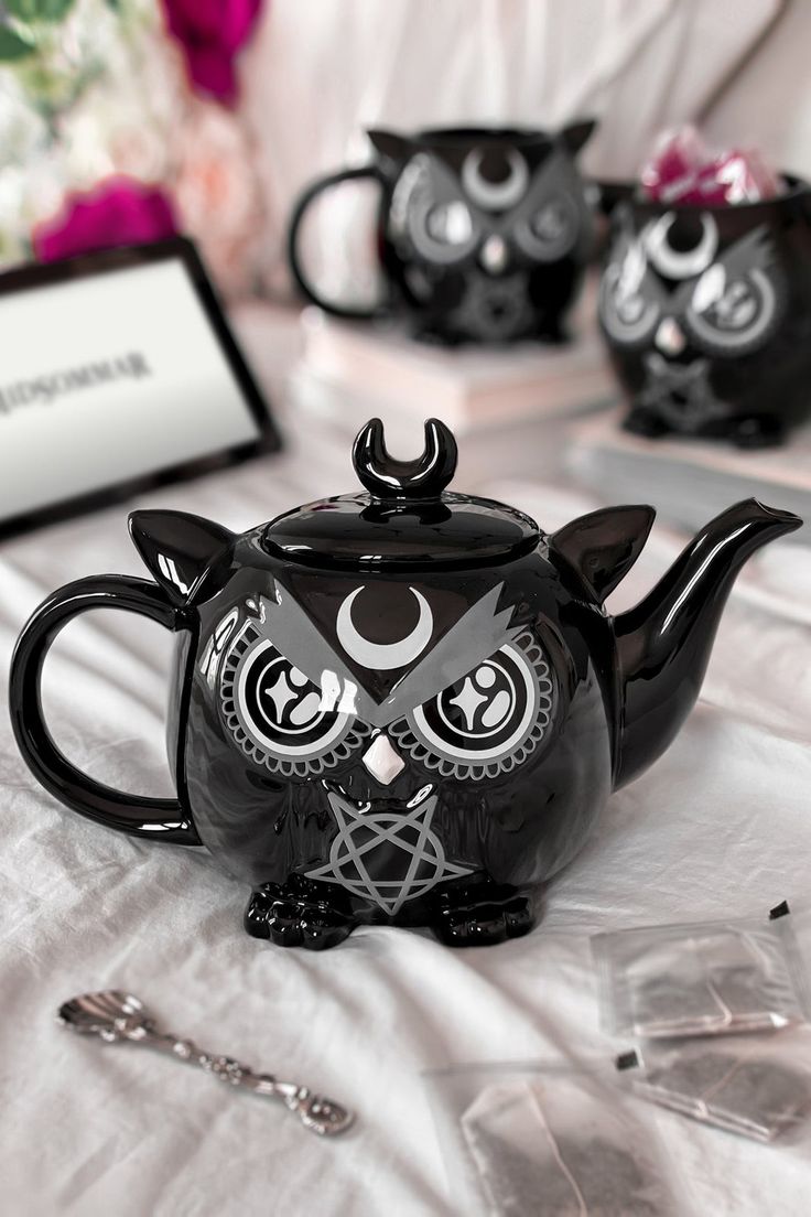 a black teapot with an owl face on it sitting on a white tablecloth