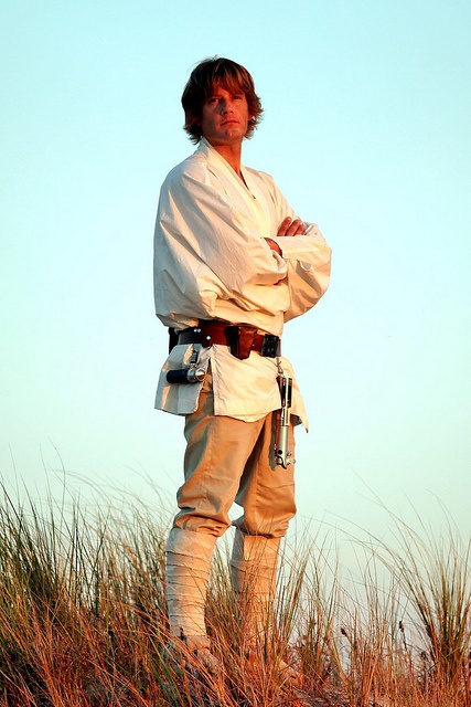 a man standing in the sand with his arms crossed and wearing a white outfit on