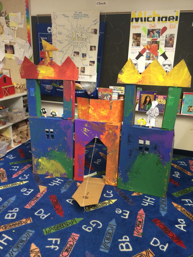 some very pretty little houses made out of cardboard and construction paper on the floor in front of bookshelves