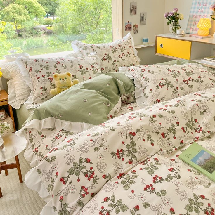 a bed with white and green comforters in a bedroom next to a window overlooking trees