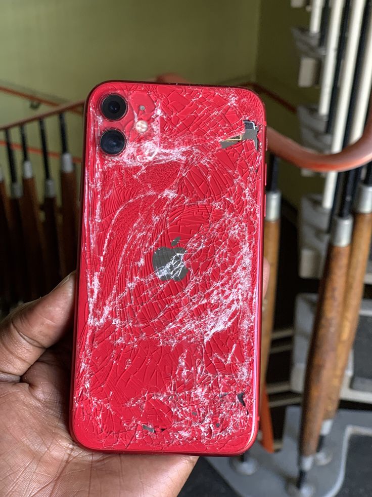 a hand holding up a red cell phone that has been broken in half and is covered with white paint