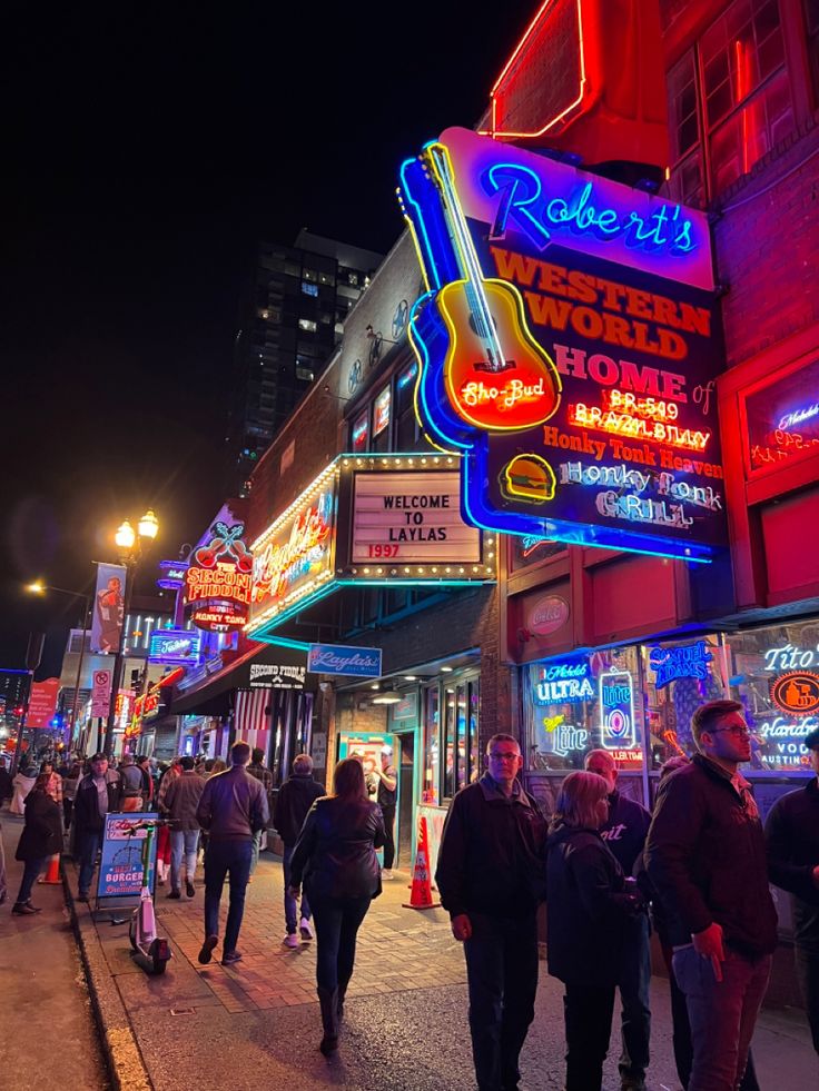 people are walking down the street in front of shops and neon signs at night time