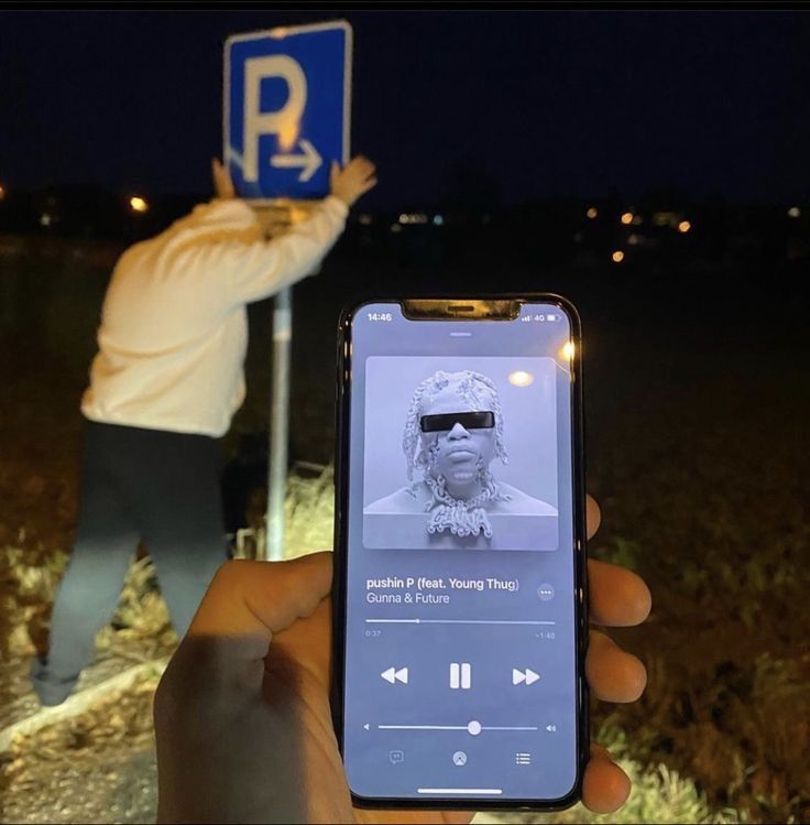 someone is holding up their cell phone to take a selfie in front of a parking sign