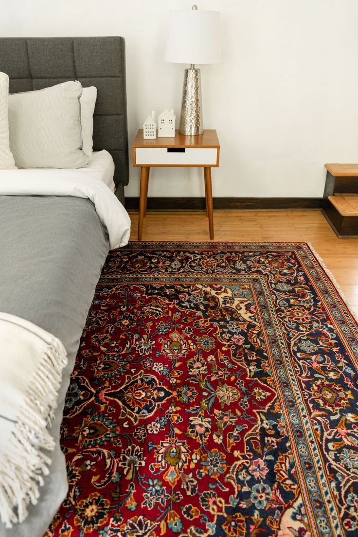 a bed sitting next to a night stand on top of a wooden floor