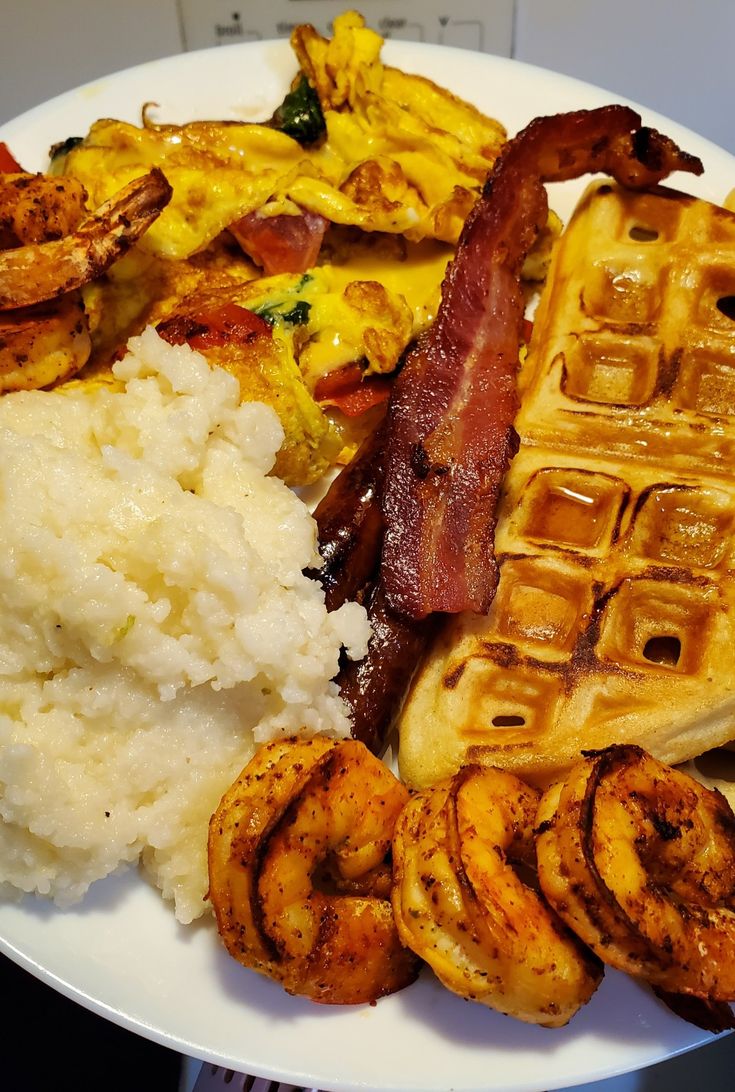 a white plate topped with waffles, bacon and other food items next to rice