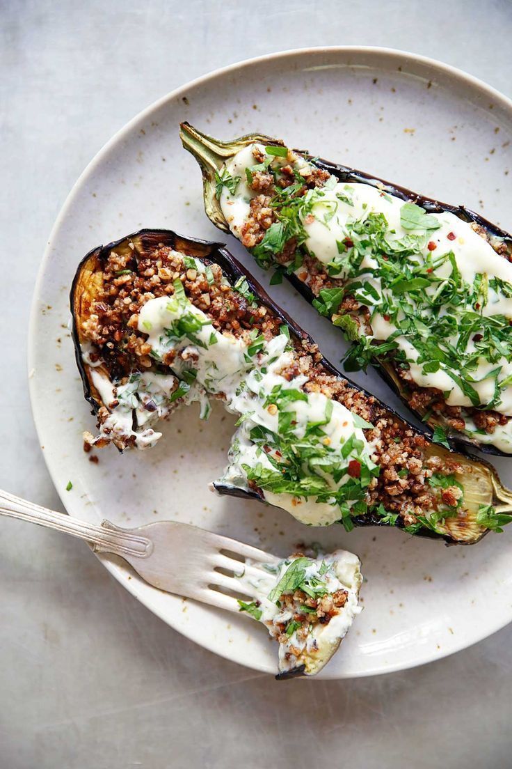 a white plate topped with two stuffed eggplant halves covered in cheese and herbs