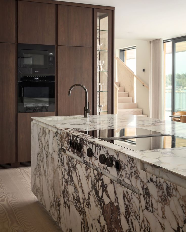 a kitchen with marble counter tops and an island in the middle of it, next to stairs