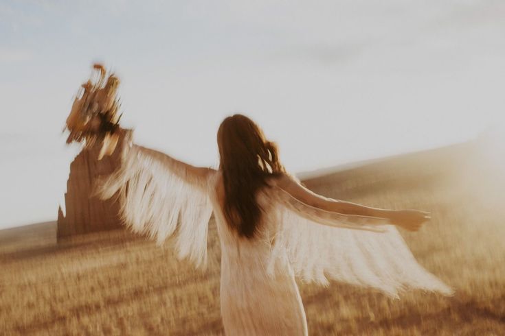 a woman in a white dress holding an angel's wings over her head while standing in a wheat field