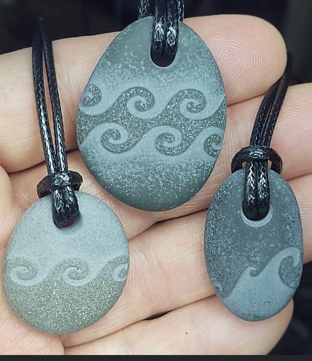 three pendants are shown in the palm of someone's hand, one is gray and the other is black