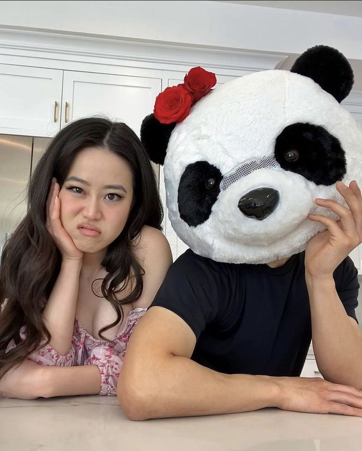 a woman sitting next to a giant panda bear with roses on it's head