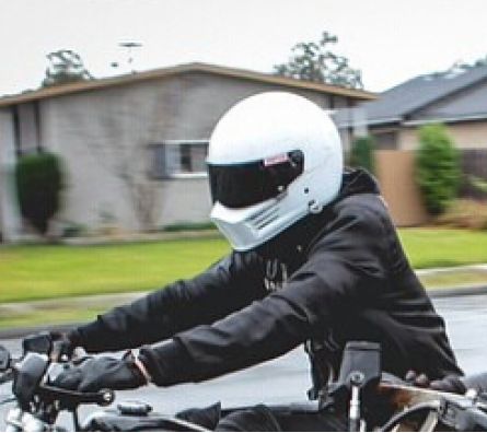 a man riding on the back of a motorcycle down a street with houses in the background