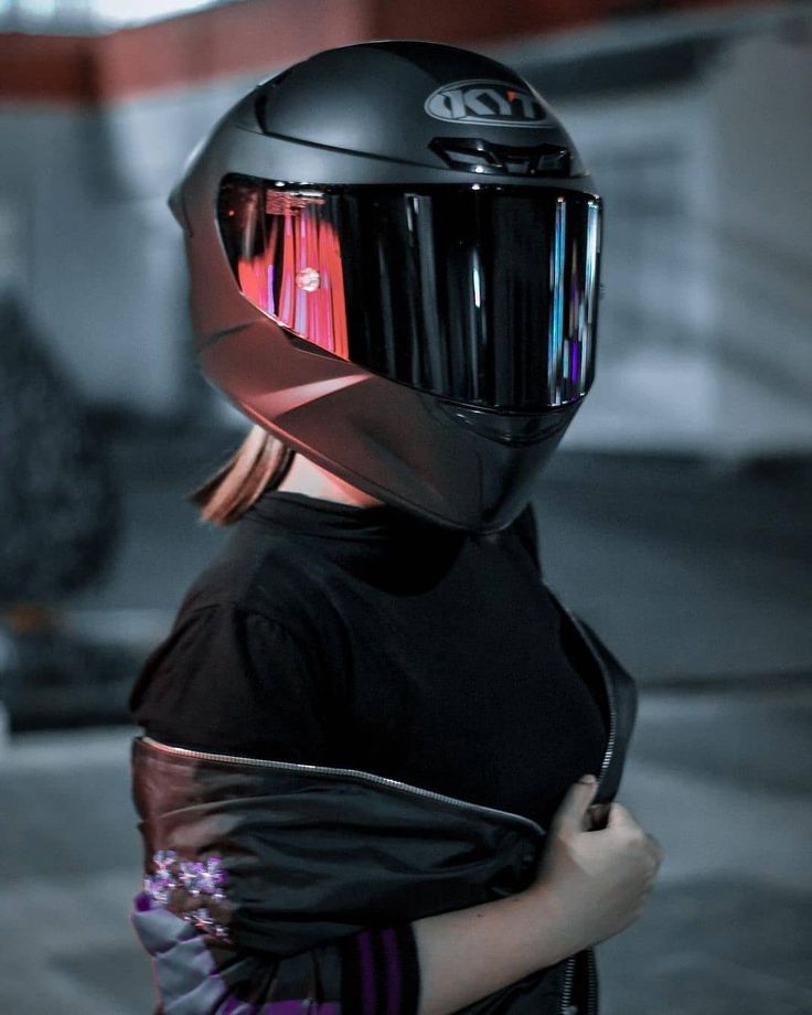 a woman wearing a black helmet and holding her back to the camera while standing in front of a building